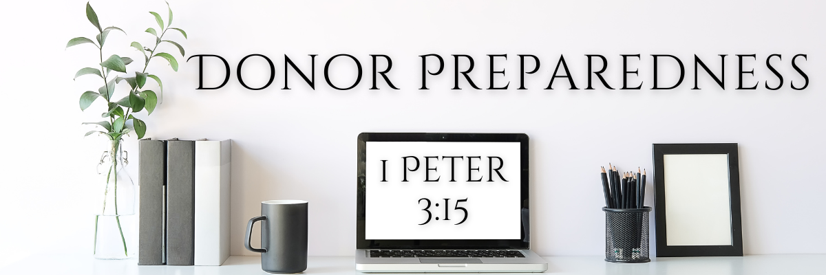 A modern, minimalist desk setup with a potted plant, books, a coffee mug, and office supplies neatly arranged. At the center is an open laptop displaying the words "1 Peter 3:15". Above the desk, large text on the wall reads "Donor Preparedness".