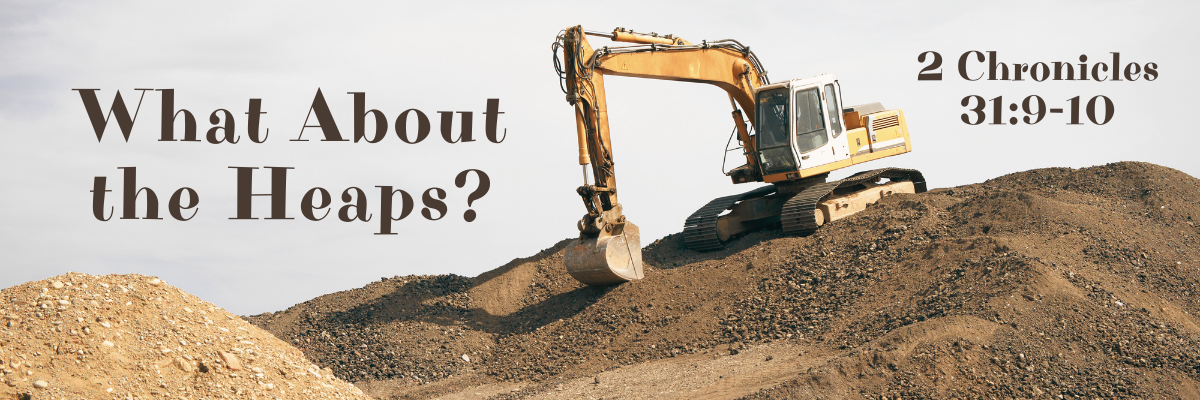 A large yellow excavator sits atop a heap of dirt and gravel under a clear sky. The text on the image reads 'What About the Heaps? – 2 Chronicles 31:9-10' in bold, brown letters.