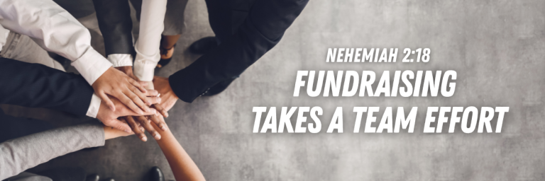 Top-down view of a diverse group of professionals in business attire stacking their hands together, with text reading Fundraising Takes a Team Effort.