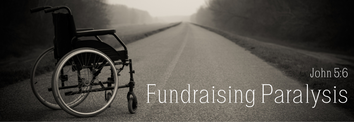An empty wheelchair sitting on a long empty road disappearing into a foggy horizon, in black and white, with the text Fundraising Paralysis and the scripture reference John 5:6 in white lettering.