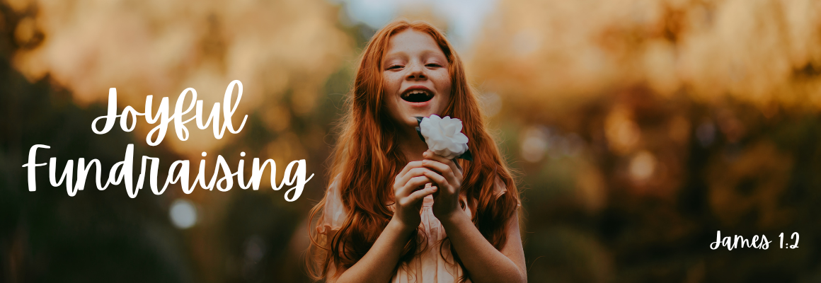 A young red-haired girl laughing joyfully while holding a white flower outdoors in warm golden light, with the text Joyful Fundraising and the scripture reference James 1:2 in white handwritten lettering.
