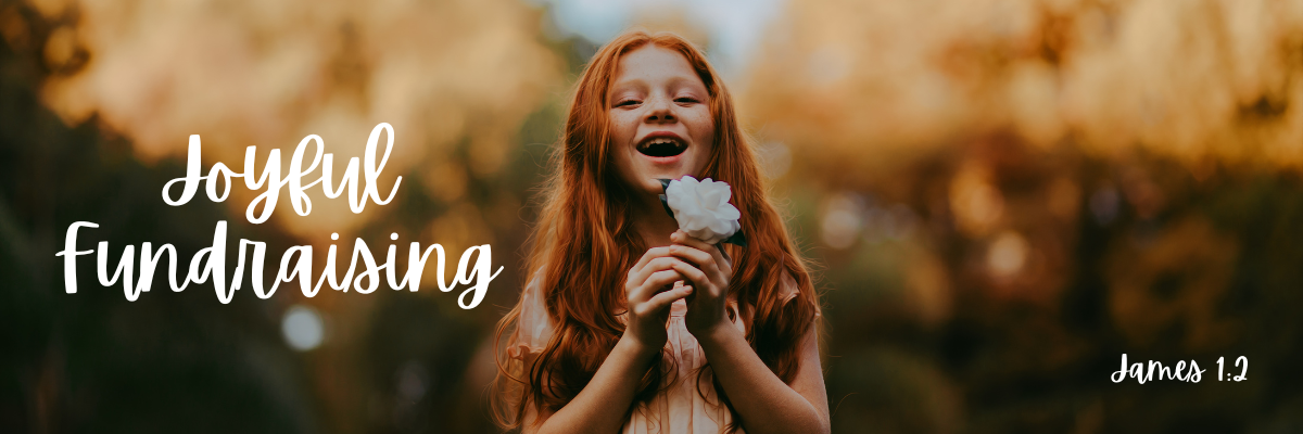 A young red-haired girl laughing joyfully while holding a white flower outdoors in warm golden light, with the text Joyful Fundraising and the scripture reference James 1:2 in white handwritten lettering.